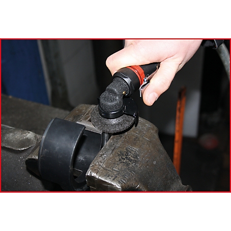 Eine Hand hält einen schwarzen Schleifer mit rotem Akzent, der einen metallischen Gegenstand bearbeitet, der in einem Schraubstock eingespannt ist.